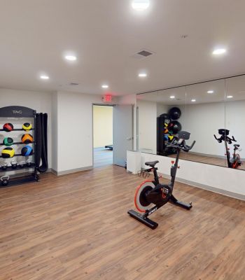 Small gym room with exercise bike, stability balls, kettlebells, and large wall mirror on wood floor.