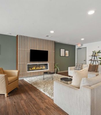 Modern living room with green accent wall, fireplace, TV, beige sofa, armchair, and wooden floor.