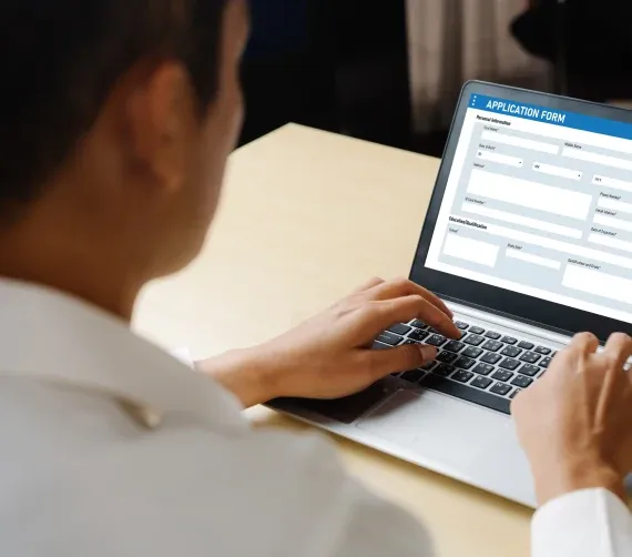 Person using a laptop to fill out an online application form at a wooden desk.